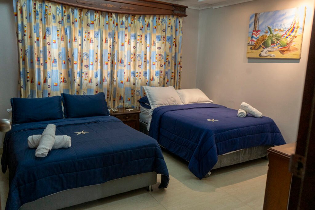 Habitación Bahía con dos camas de cobertores azules y cortinas estampadas
